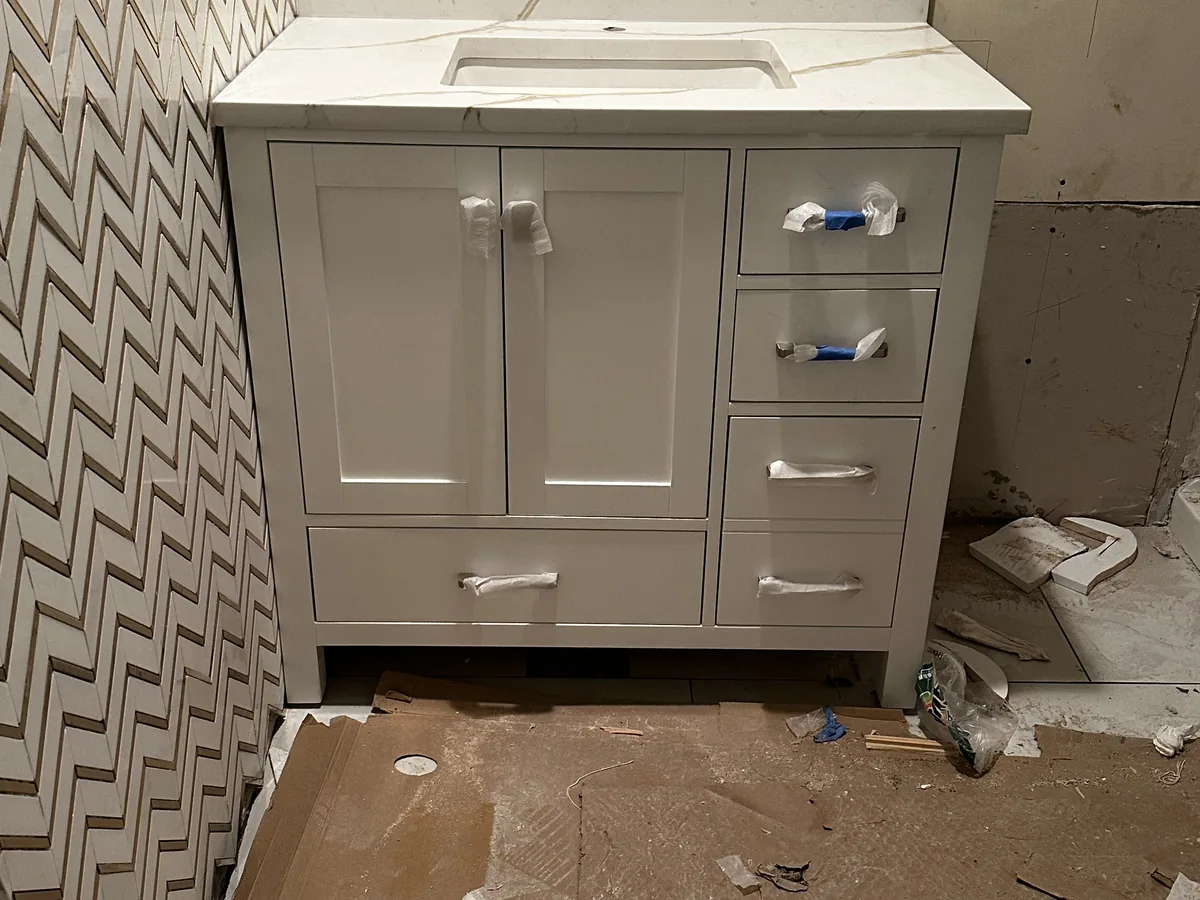 White vanity with stone top and tile finish work during a residential bath renovation